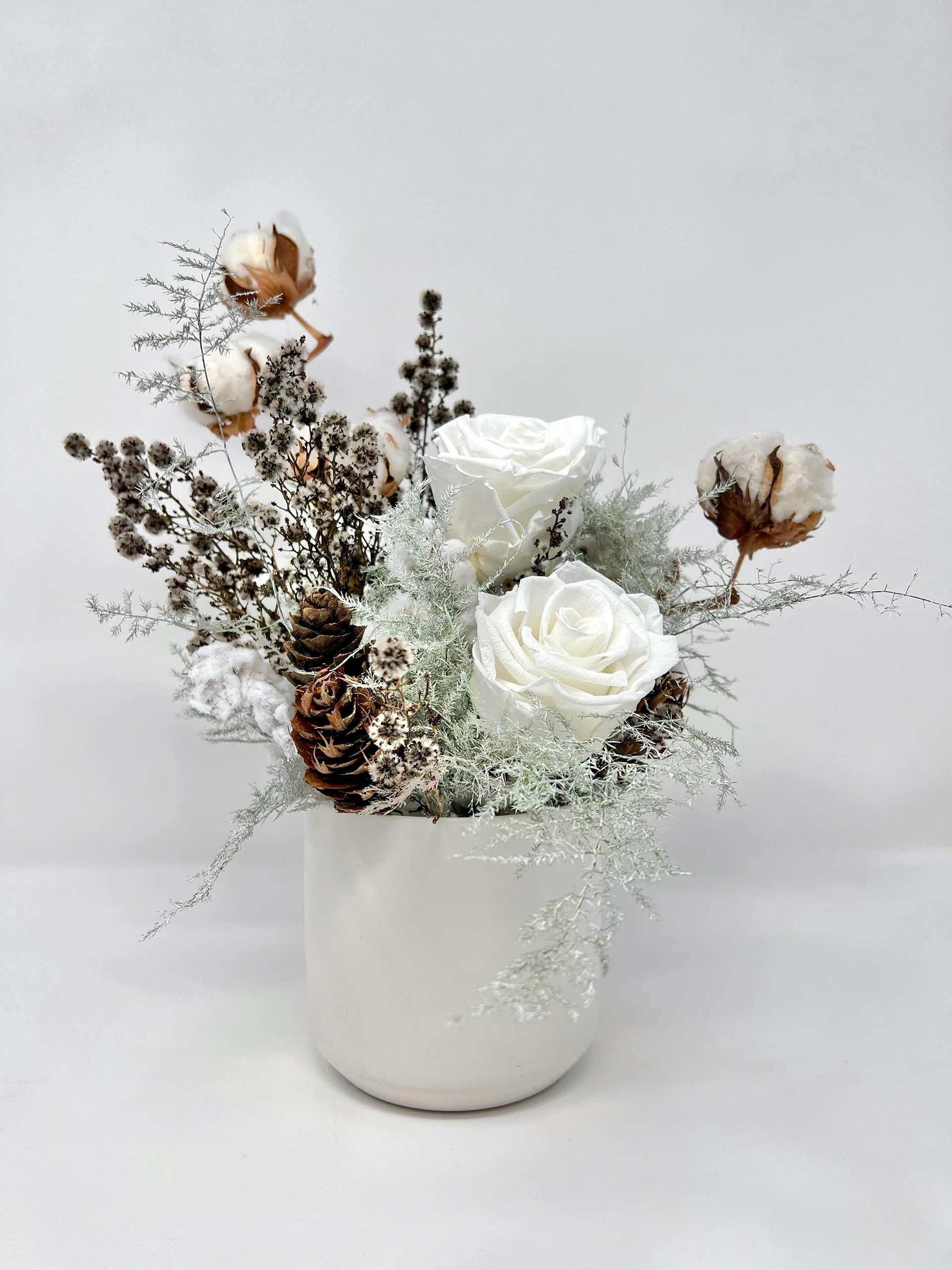 Christmas dried floral arrangement with white roses, pinecones, and cotton stems in a white vase by Floba.