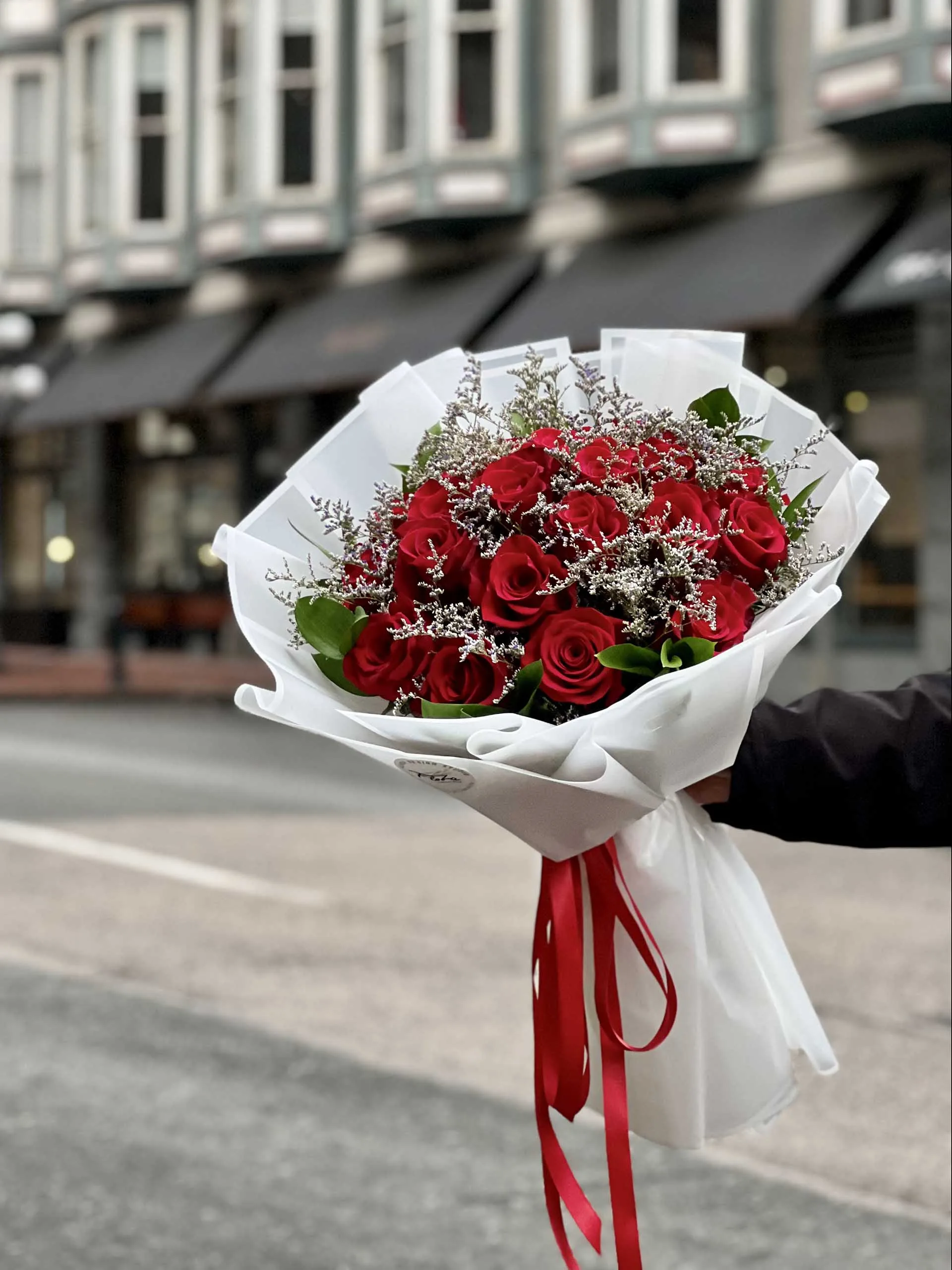 Crimson Romance Bouquet featuring red roses with delicate white filler flowers, wrapped in elegant white paper and tied with a red ribbon—available in customizable sizes of 18, 24, or 36 roses.