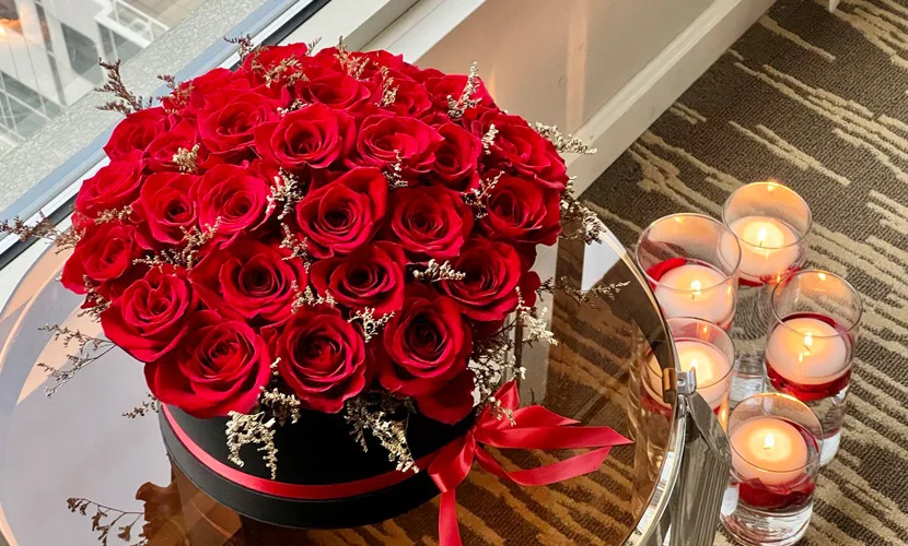 Midnight Rose Symphony featuring luxurious red roses with golden accents arranged in a black box, beautifully displayed with candles for an elegant and romantic setting.