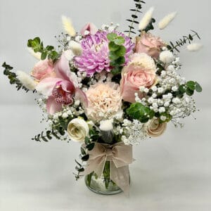 Blushing Serenity Arrangement featuring a serene mix of pink, white, and cream blooms in a decorative glass vase, tied with a ribbon.