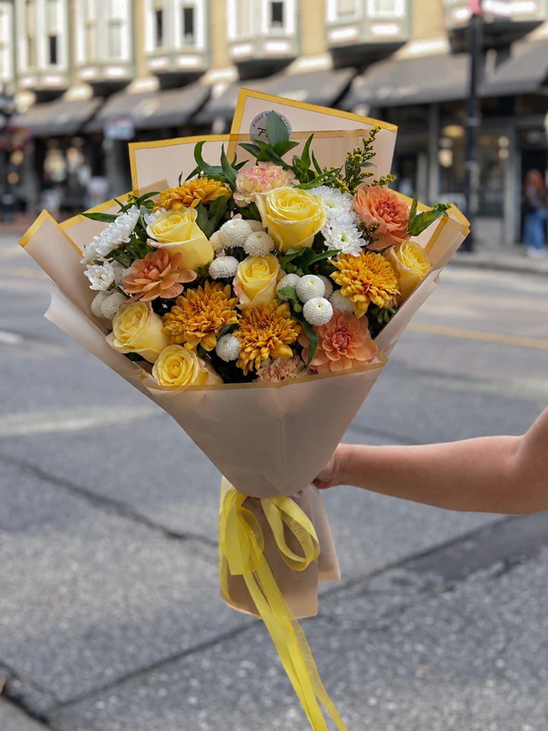 Autumn Harvest Bouquet Autumn Harvest Bouquet held outdoors with yellow roses, white blooms, peach flowers and trailing yellow ribbons