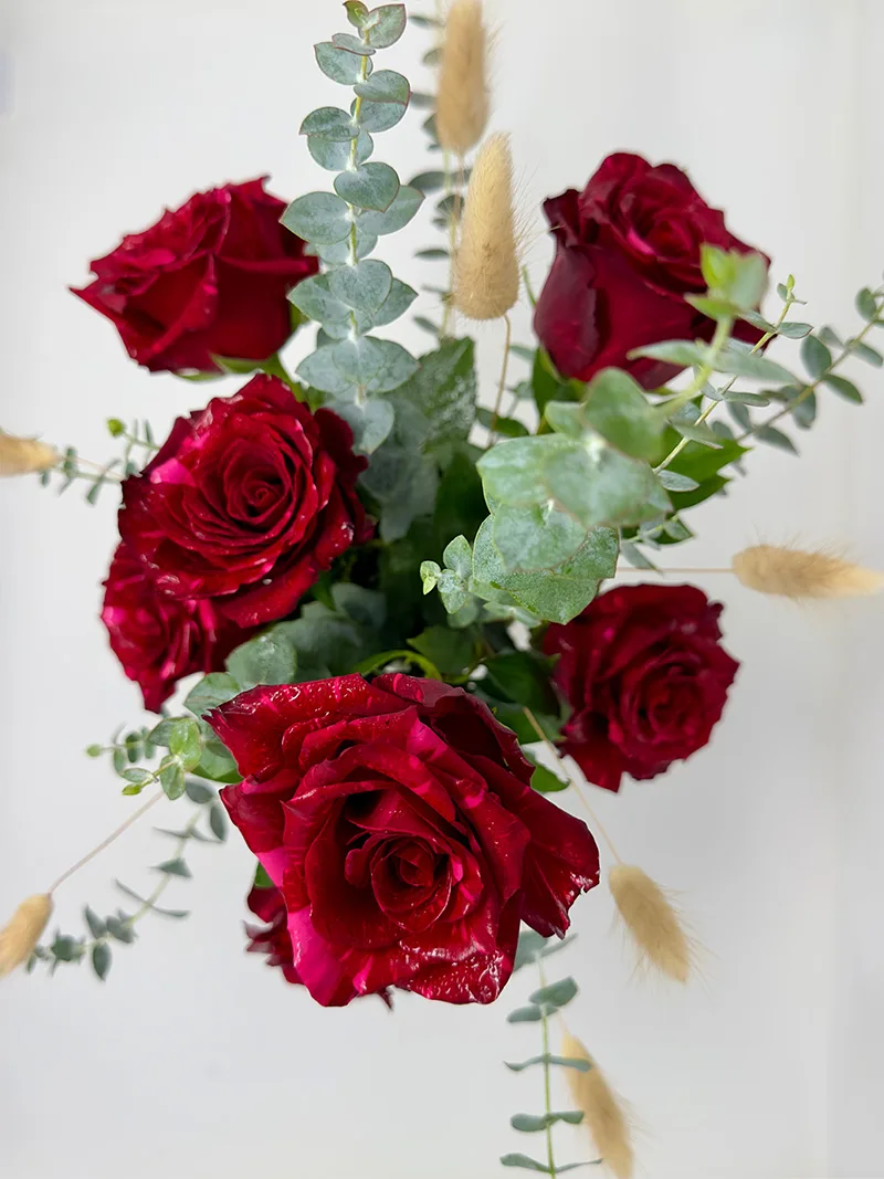 Top View - Crimson Radiance Vase Top view of Crimson Radiance Vase with six deep red roses, eucalyptus leaves, and bunny tails in a ceramic vase