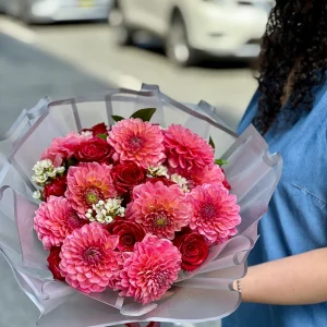 Pink dahlia bouquet with red roses and white waxflower in translucent wrapping