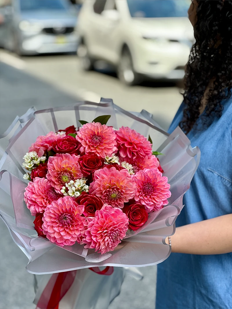 Pink dahlia bouquet with red roses and white waxflower in translucent wrapping