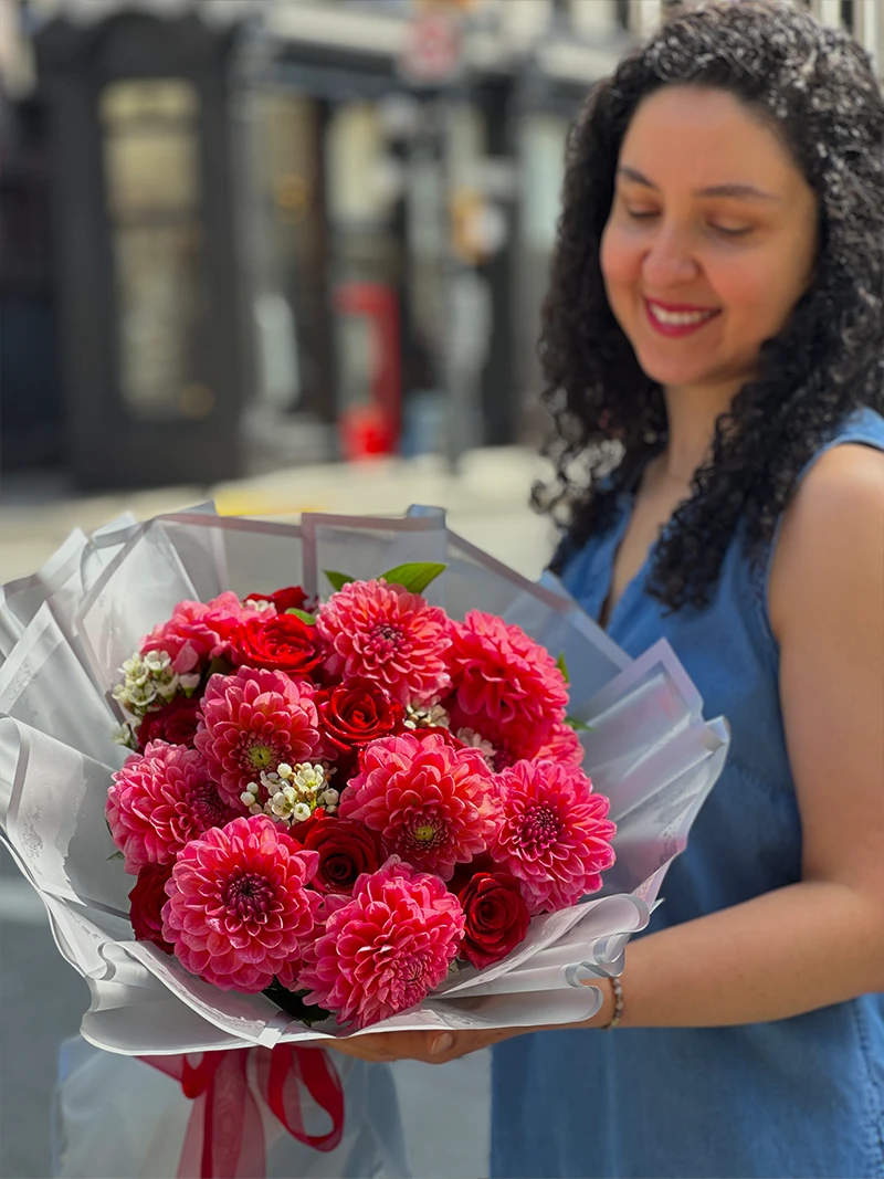 Woman holding a bouquet of pink dahlias and red roses outdoors