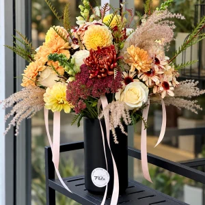 Autumn Muse arrangement with yellow dahlias, ivory roses, burgundy flowers and soft grasses in a black vase