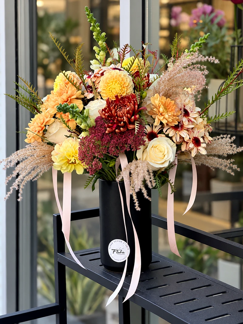 Autumn Muse arrangement with yellow dahlias, ivory roses, burgundy flowers and soft grasses in a black vase